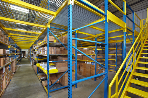 Pallet rack components are used to support a work platform above, with beam levels below for standard pallet storage. The upright frames can extend through the work platform floor to provide more storage levels above.